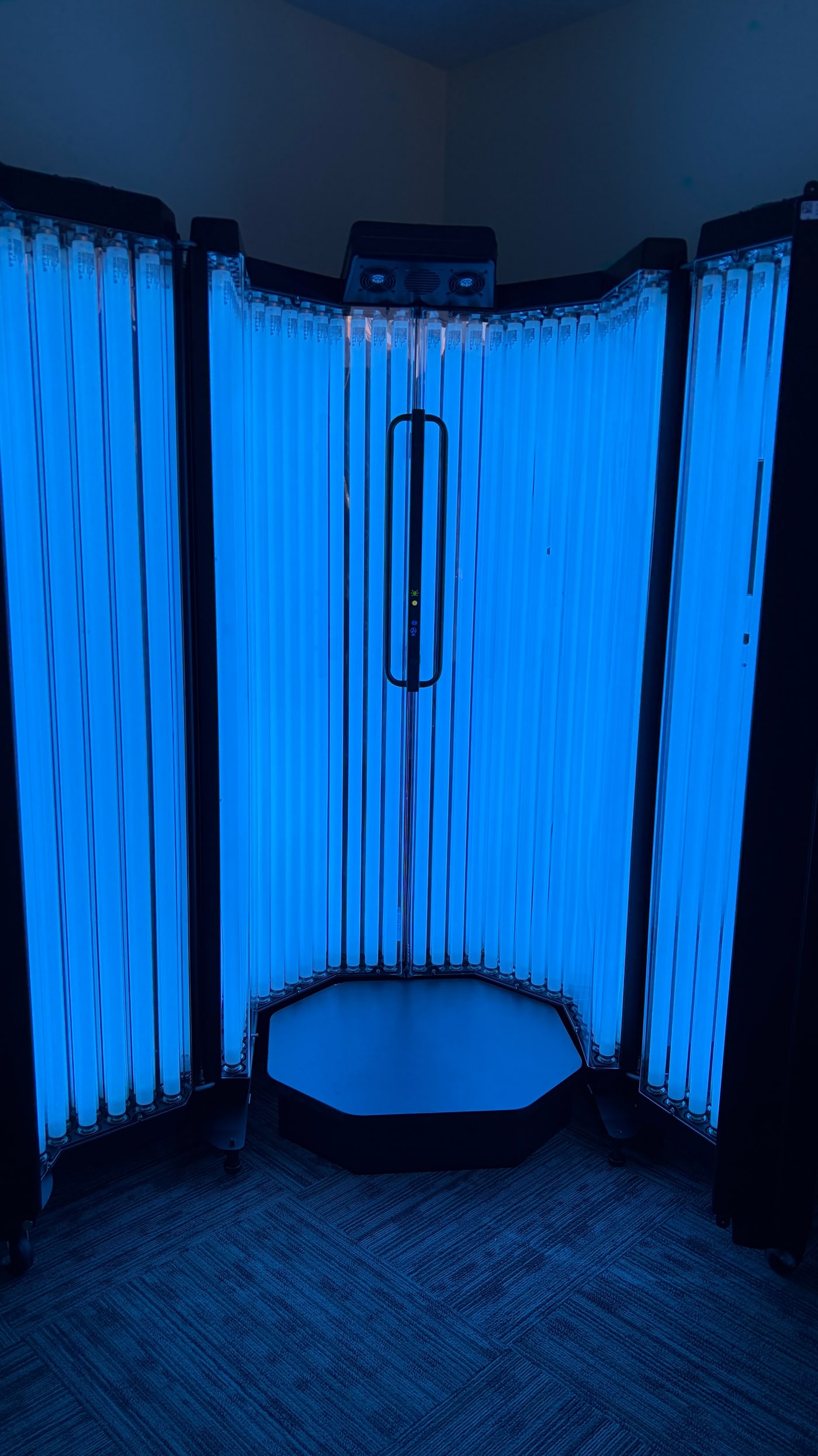 A patient's view of the full narrowband UVB phototherapy booth with its lamp walls illuminated in bright blue light